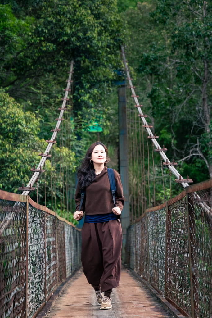 cô gái dạo bước trên cầu treo tại làng kon tu ma với rừng cây phía sau và con suối phía dưới trong các tour trekking măng đen