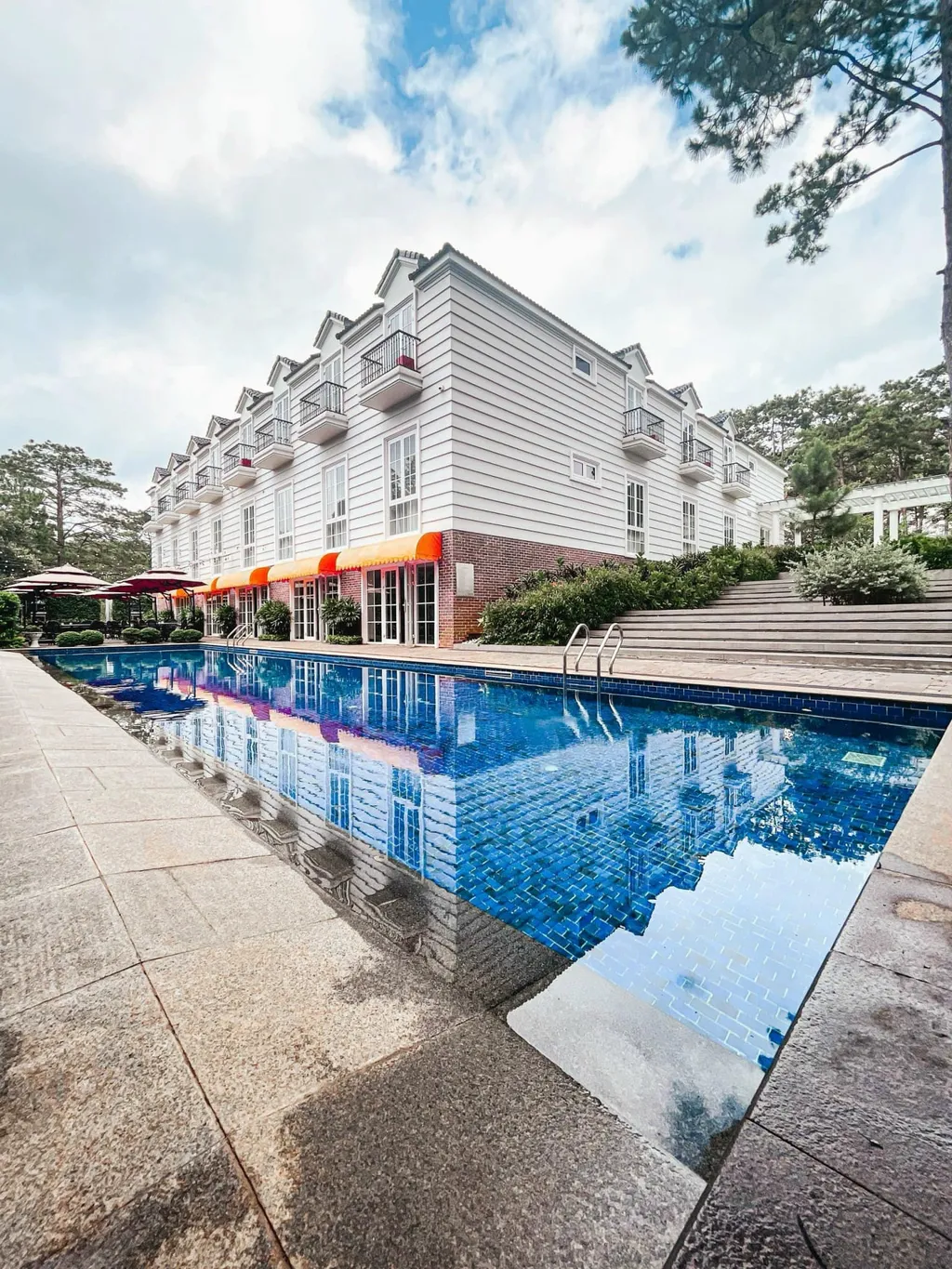 Khách sạn Măng Đen Golden Sun với mặt tiền trắng, vườn hoa và hàng thông, phù hợp khách muốn nơi ở chỉn chu gần trung tâm
