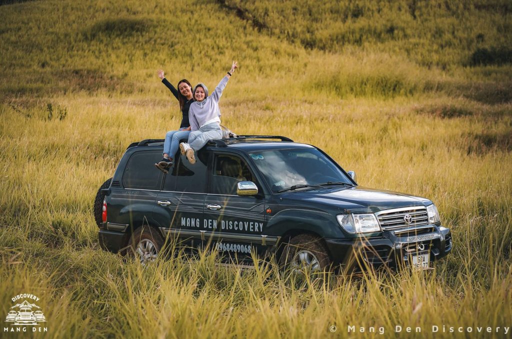 cặp đôi ngồi trên nóc xe chụp ảnh giữa cánh đồng cỏ vàng trong ánh chiều tà trong tour 3n2d măng đen