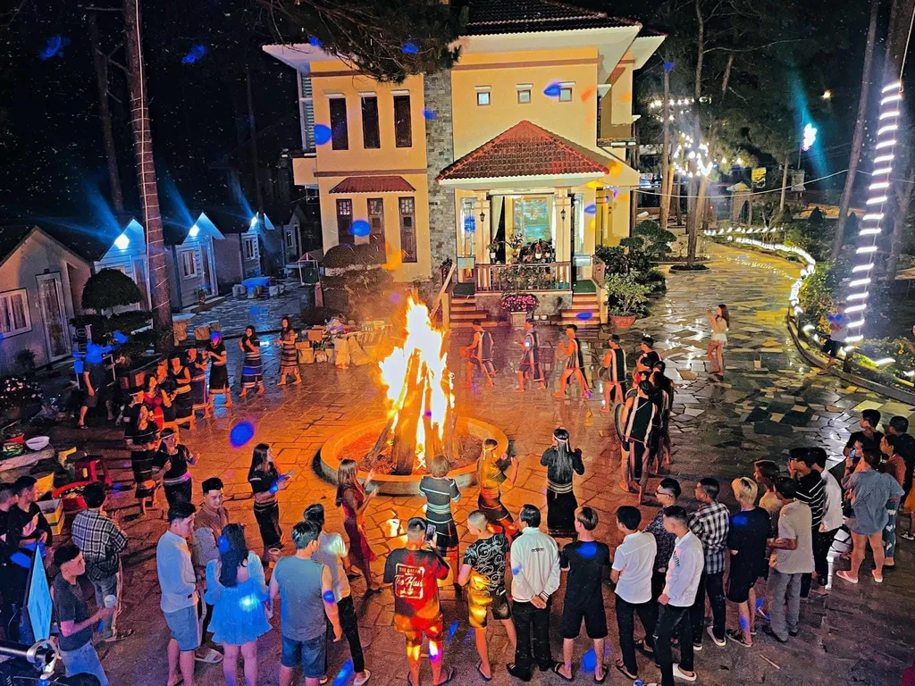 Sân lửa trại tại Henisi Măng Đen với nhóm khách quây quanh buổi tối, phù hợp đoàn đông muốn không gian sinh hoạt chung