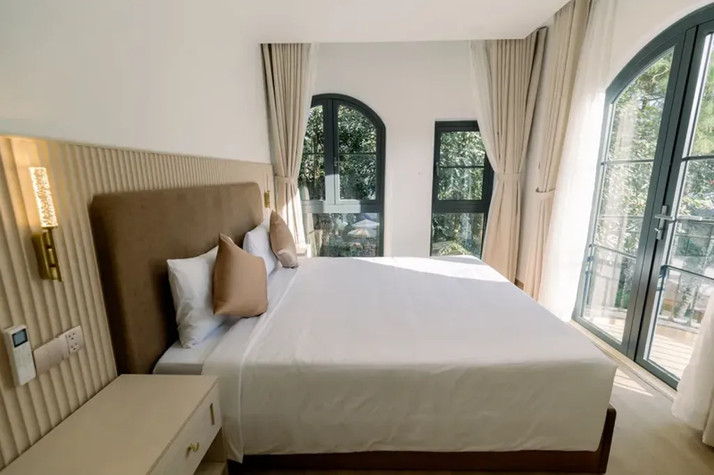 Phòng ngủ Veluna Hotel Măng Đen có giường đôi, cửa kính lớn và ánh sáng tự nhiên cho khách cần khách sạn 3 sao dễ ở