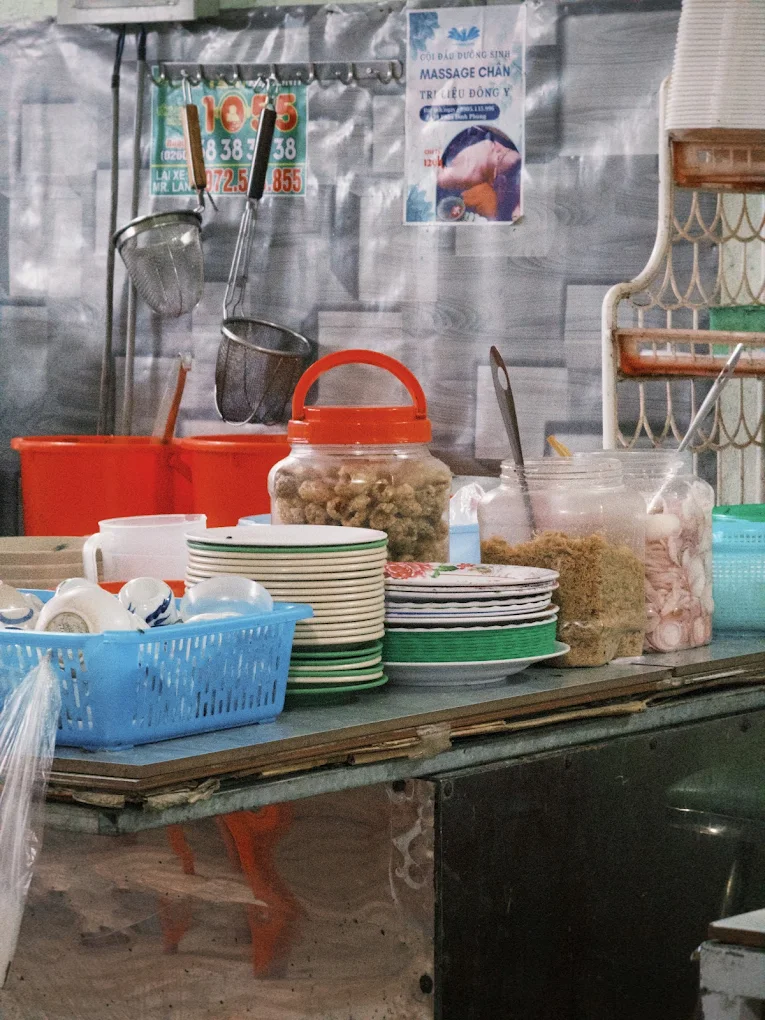 Quầy chuẩn bị topping tại Qu&aacute;n B&agrave; Bảy Măng Đen với b&aacute;t đĩa, t&oacute;p mỡ v&agrave; h&agrave;nh ng&acirc;m